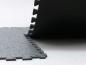 Preview: The image shows a black, textured surface made of thick mats stacked at one edge. One mat is slightly lifted, while the other is flat. The surface has a rough texture.