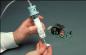 Preview: One hand is holding a syringe filled with a white material, while the other hand works on a green circuit board with various electronic components.