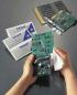 Preview: In the picture, two hands can be seen holding a circuit board and cleaning it with a cloth. In the background, there are three packs of Safepad and a second circuit board.