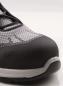 Preview: The image shows the tip of a gray shoe with a solid, black cap. The upper material is made of a loose, breathable fabric. Laces run across the shoe.