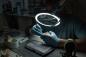 Preview: A person is wearing gloves and working under a magnifying lamp. In front of them lies a processed model. The room is dimly lit to enable precise work.