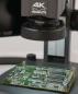 Preview: Das Bild zeigt eine grüne Leiterplatte unter einem Mikroskop mit der Aufschrift "4K Makrolite". Die Platine hat verschiedene elektronische Bauteile und ist auf einem Tisch platziert.