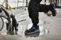 Preview: A foot stands on a wet floor, surrounded by tools and hoses. The shoe is black with blue accents, the pants are dark and protect against moisture.