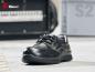 Preview: The image shows a black safety shoe with laces. It features a sturdy, padded cap and a non-slip sole. In the background are blurred industrial elements.