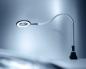 Preview: The image shows a flexible desk lamp with a round, magnifying light. The neck of the lamp is bendable and it stands on a stable, black base. The background is in soft shades of gray.
