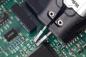 Preview: The image shows a green circuit board with electronic components. Two pliers precisely grip a spot on the board. Detailed circuits are visible.
