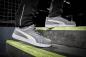 Preview: Das Bild zeigt graue Sportschuhe auf einer Treppe. Die Schuhe sind flach, mit einer dicken weißen Sohle, und die Person trägt schwarze Hosen mit weißen Akzenten.