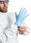 Preview: Ein Mann in einem weißen Schutzanzug zieht sich einen blauen Gummi-Handschuh an. Er trägt eine Schutzbrille und konzentriert sich auf die Aufgabe.