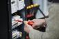 Preview: A person is holding a screwdriver and working on an electrical panel, which is equipped with multiple devices and colorful cables.