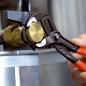 Preview: Ein Handwerker benutzt eine verstellbare Zange, um eine runde, goldene Schraube an einem silbernen Metallzylinder zu befestigen. Der Fokus liegt auf den Werkzeug und der Schraube.
