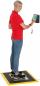 Preview: A person with short, blonde hair is wearing a red shirt and jeans. They are standing on a platform and holding a digital device in their hand. The background is neutral.