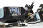 Preview: The image shows a soldering iron tool being used on a circuit board as smoke rises. In the background, there is a soldering station with digital displays.