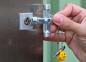 Preview: A hand holds a silver key in a square, silver lock. Attached to the key is a yellow plastic shape with a chain. The background is green.