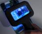 Preview: In the picture, you see a hand holding a magnifying glass with an illuminated display over a circuit board. The board displays various electronic components in bluish light.