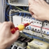 Preview: Eine Person arbeitet an einem Schaltschrank mit elektrischen Komponenten. In einer Hand hält sie einen Schraubendreher. Mehrere Sicherungen und Kabel sind sichtbar. Eine technische Umgebung.