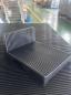 Preview: The image shows a black, rectangular block with a raised back. The surface is ridged and consists of parallel stripes. It is situated on a flat, even surface.