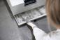 Preview: A person in a white top is pulling out a drawer from a gray device. The drawer is gray and shows signs of dirt or dust. The floor is also gray.