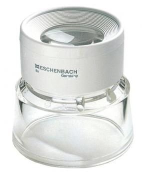 The image shows a magnifying glass in a compact, round design. At the top is a clear lens insert, below which is a slightly curved base made of transparent plastic. The surface is predominantly white.