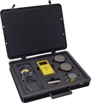The image shows an open, black suitcase. Inside, there is a yellow device with a display, two round buttons, a cable, and another device. Everything is neatly arranged.