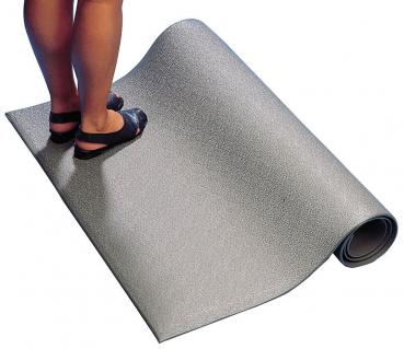 The image shows a section of a gray, textured mat material with a pair of feet wearing black sandals standing on it. The mat is slightly rolled up at one end.