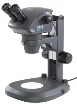 The image shows a microscope with two objectives and a stable base. It has a gray body and various controls on the side to adjust the settings.