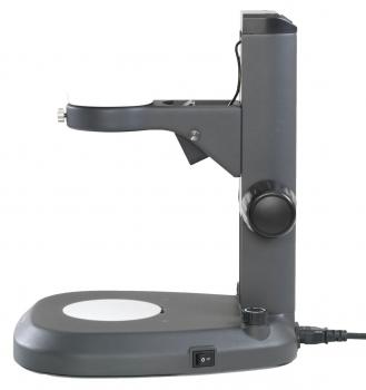 The image shows a gray magnifying device on a stable base. It has a short arm with a lens and controls for adjustment. A switch is located on the bottom.
