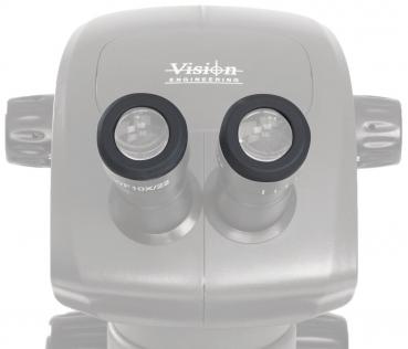 The image shows a microscope with two round eyepieces. The surface is smooth and oval. At the top, it reads "Vision Engineering". It is a technical device for magnifying objects.