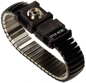 The image shows a black, metallic bracelet with a flexible, springy structure. In the center, there is a rectangular clasp marked with the inscription "OPEN HERE".