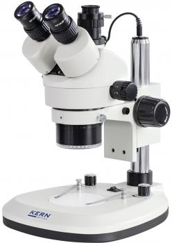 The image shows a microscope in white and silver. It has two eyepieces on top, a long body, and various adjustment options on the side. The base is stable and flat.