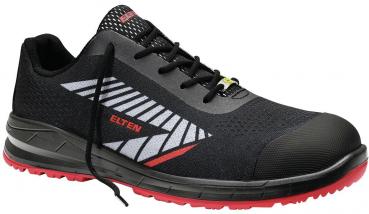 The shoe is a black, slightly sporty work shoe with gray and red accents. It has a reinforced toe cap, elastic laces, and a non-slip sole.
