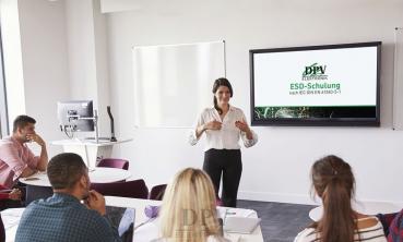 In a bright room, a woman leads a training session. She stands in front of a screen titled 
