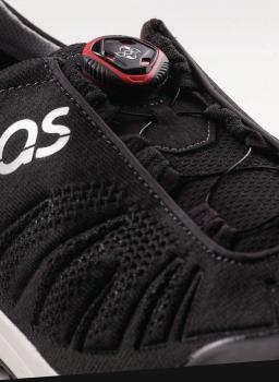 The image shows a black sports shoe with a tight, breathable material and lacing adjusted by a red-black push button. A logo is visible.