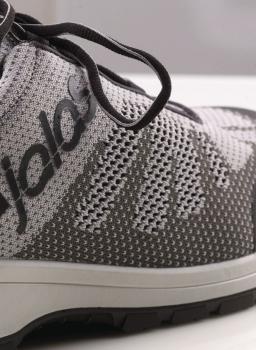 The image shows a gray sports or running shoe. It features a breathable, knitted upper with a subtle pattern and gray laces. The shoe has a light-colored sole.