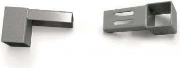 The image shows two metal parts in shades of gray. On the left, a block-shaped element with a short protrusion. On the right, a long element with a square cutout and two narrow holes.