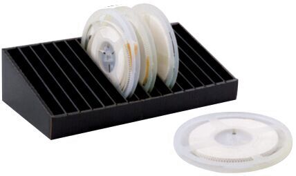 The image shows a black storage box with compartments for several transparent film reels. One reel is lying next to it. The reels are circular with a central opening.