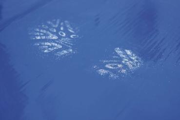 On a smooth blue surface, two footprints are visible, left with a white material. The prints show the shape of shoes.