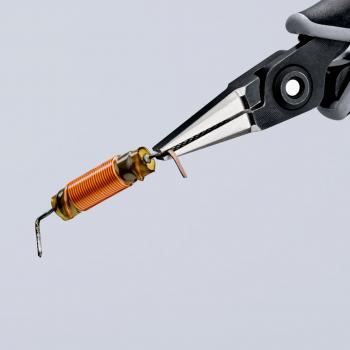 Zwei Zangen greifen einen kleinen, zylindrischen Bauteil mit orangefarbenem Draht und metallischen Enden. Der Hintergrund ist hell und wenig detailliert.
