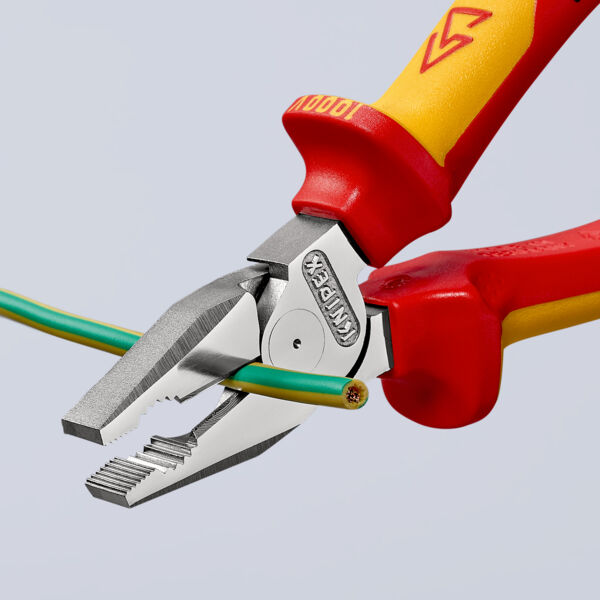 The image shows a pair of pliers with red and yellow handles. It is gripping two electrical wires, one green and one yellow. The pliers have a flat, sharp edge for cutting.