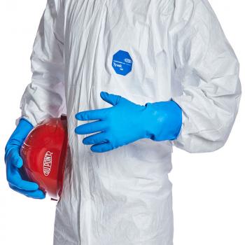 Das Bild zeigt eine Person in einem weißen Schutzanzug mit blauen Handschuhen. In einer Hand hält sie einen roten Helm, während die andere Hand offen ist.