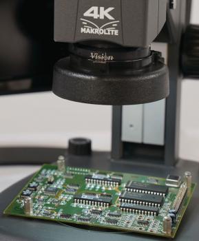 Das Bild zeigt eine grüne Leiterplatte unter einem Mikroskop mit der Aufschrift "4K Makrolite". Die Platine hat verschiedene elektronische Bauteile und ist auf einem Tisch platziert.
