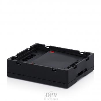 Das Bild zeigt eine schwarze, quadratische Elektronikbox mit leicht erhöhten Kanten. Die Oberfläche ist schlicht und matt, mit Aussparungen an den Seiten. Der Hintergrund ist weiß.
