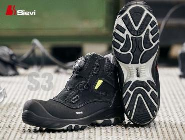 The image shows a pair of black safety boots with a modern design. The sole has a diamond-patterned profile for better grip. A yellow accent color is visible.