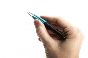 A hand is holding a blue pen with a black grip area. The pen has a pointed tip pointing upwards. The background is white and neutral.