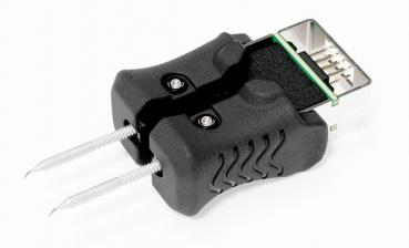 The image shows an electrical measuring device with two metal probes and a black plastic casing. At the top, there is a slot with pins used for electrical connections.