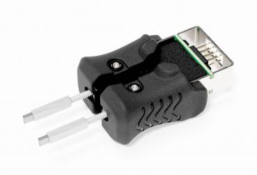 The image shows a black plug with a rectangular connection on top and two metallic pins protruding from the sides. The surface is ribbed and there are small screws.