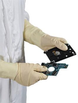 A person in white gloves is holding two parts of a computer drive. The upper part is black and has a round opening, the lower part is green with fine circuits.