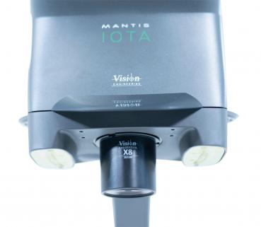 Das Bild zeigt einen Mantis IOTA, ein kompaktes, tragbares Sehhilfe-Gerät. Es hat eine graue Oberfläche mit runden Objektiven und einem stabilen Sockel. Ideal für bessere Sicht bei Nah- und Fernobjekten.