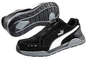 The image shows a black sports shoe with gray and white accents. It features a flat sole with good tread and a unique lacing mechanism instead of traditional laces.
