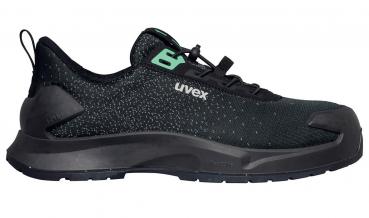 Der Schuh ist ein schwarzer, sportlicher Sneaker mit einer strukturierten Oberfläche. Er hat eine verstärkte Gummisohle und eine grüne Logoschrift an der Seite.