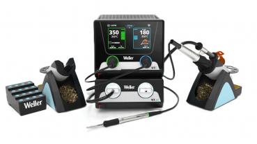 The image shows a soldering station with a control unit and two soldering tips. The control unit has a display with temperature readings. Next to the unit, there are soldering tin and cleaning materials.